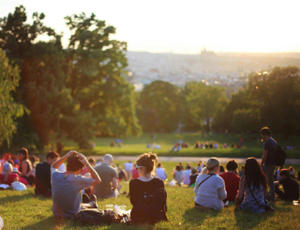 Crowd seated in a field, surrounded by trees, facing the setting sun